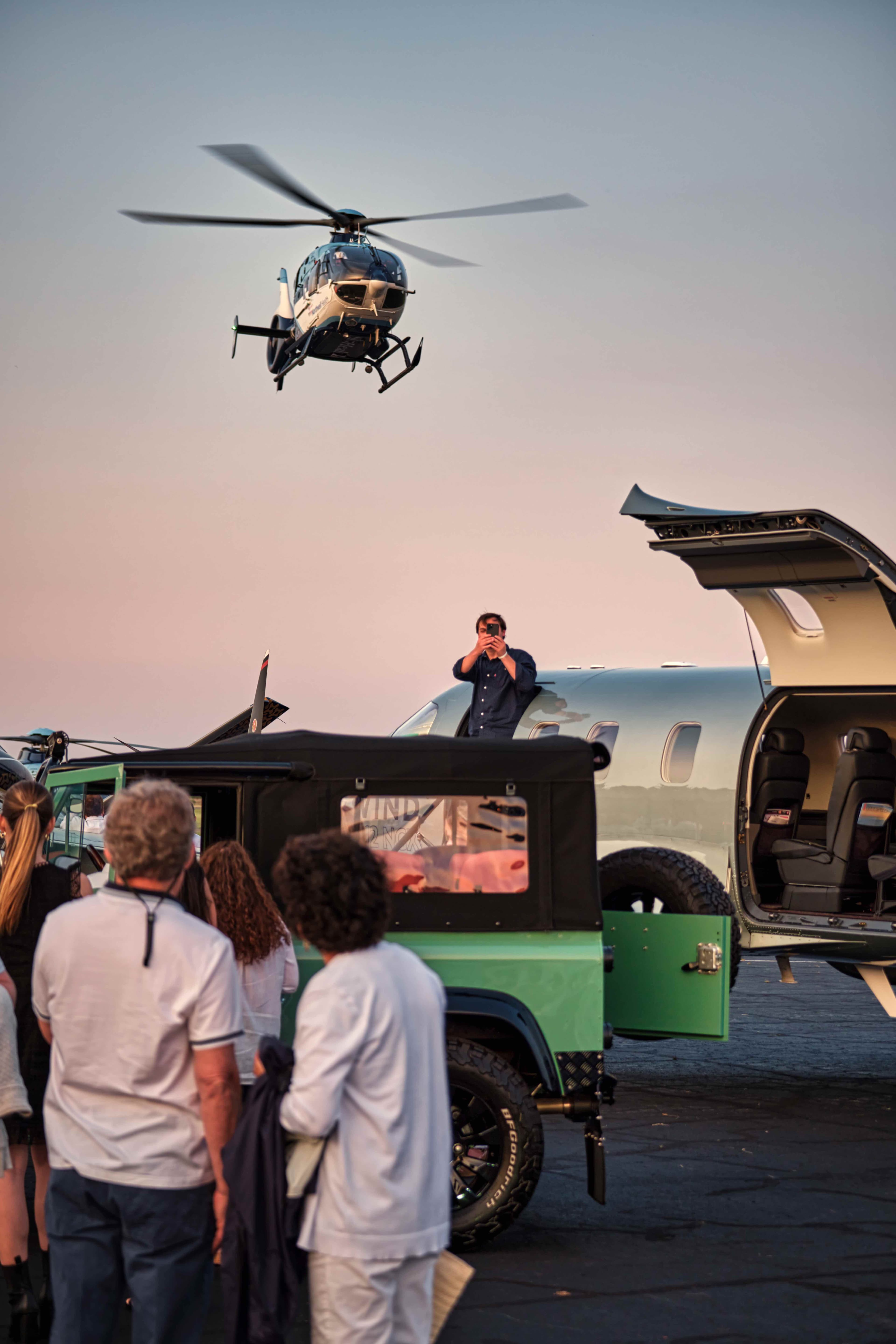 Helicopter arriving at Wings Wheels Water event with private jet and vintage vehicles